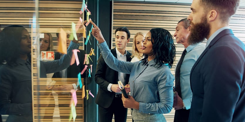 two women and three men looking at business capabilities examples on post-it notes